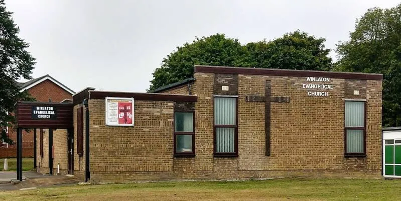 The front of the church from the road, with its sign and cross on the wall